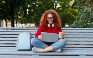 Happy female student enjoying coffee and using laptop